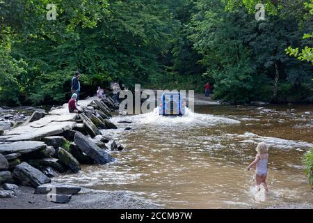 Ein Auto fährt durch den Fluss Barle an der Klappbrücke Tarr Steps im Exmoor Nationalpark, Somerset Stockfoto