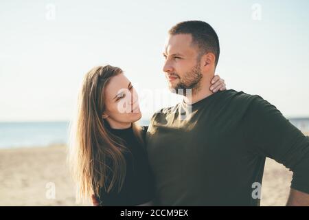 Schöne Frau voller Liebe suchen zu schönen überzeugten Mann umarmt sie. Junges erwachsenes Paar, das an der Küste steht und sich umarmt. Millennial männlich und weiblich posiert am Strand an sonnigen Tag Stockfoto