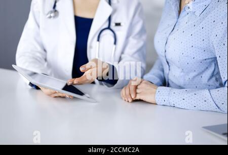 Unbekannte Ärztin zeigt ihrem Patienten eine Beschreibung der Medikation, während sie zusammen am Schreibtisch im Schrank in einer Klinik sitzt. Weiblich Stockfoto