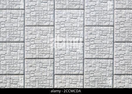 Hellgraue Quadrate aus gemustertem Stein. Die Steine enthalten unregelmäßige Rechtecke. Helles Sonnenlicht. Stockfoto