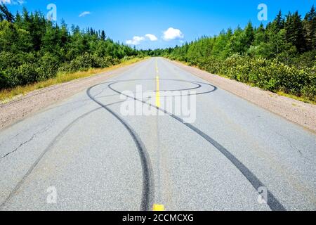 Mehrere Gleitspuren auf einer zweispurigen Autobahn. Bäume säumen die Straße und der Himmel ist mostky blau oben. Heller, sonniger Tag. Stockfoto