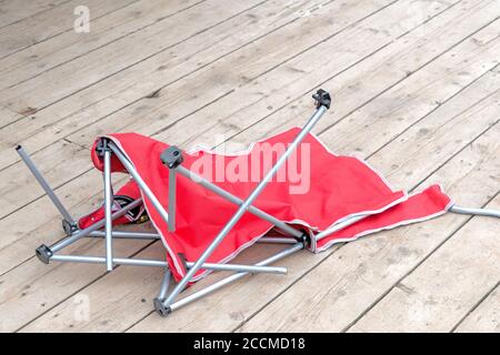 Ein roter Stoff gebrochen Strand oder Liegewiese auf einem Holzdeck. Die Metallbeine sind gebrochen und in Unordnung. Stockfoto