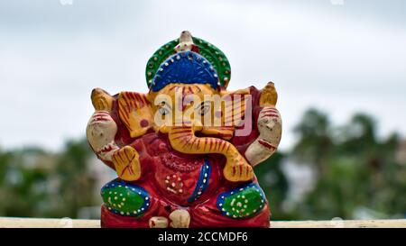 Hölzerne bunte Miniatur lord ganesha Idol mit verschwommenem Himmel und Baumhintergrund Stockfoto