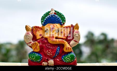 Hölzerne bunte Miniatur lord ganesha Idol mit verschwommenem Himmel und Baumhintergrund Stockfoto