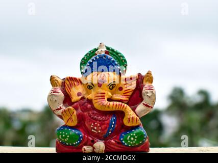 Hölzerne bunte Miniatur lord ganesha Idol mit verschwommenem Himmel und Baumhintergrund Stockfoto