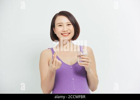 Junge schwangere Frau hält Glas Wasser und Pille. Stockfoto