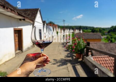 Mann hält ein Glas Rotwein mit vielen bunten Alte traditionelle Kellerei in Villanykovesd in einem ungarischen Wein Region genannt Villany Stockfoto