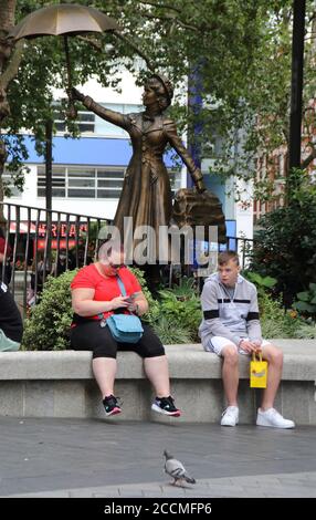 London, Großbritannien. August 2020. Zwei Personen sitzen auf dem Leicester Square mit der Bronzestatue Mary Poppins im Hintergrund.nach der Lockerung der Lockdown-Maßnahmen während der Covid-19-Krise scheinen viele Dinge mit den zusätzlichen sozialen Distanzierungen und Facemask-Vorkehrungen wieder fast normal. Kredit: Keith Mayhew/SOPA Images/ZUMA Wire/Alamy Live Nachrichten Stockfoto