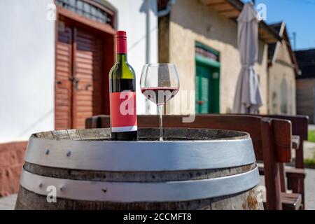 Glas Rotwein mit Flasche auf einem Fass mit Viele bunte alte traditionelle Weinkeller in Villanykovesd in einem ungarische Weinregion genannt Villany Stockfoto