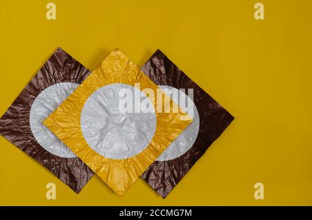 Drei quadratische Stücke von farbigen Folie auf gelb. Folienstücke braun und gelb mit einem weißen Kreis. Abstrakter Hintergrund. Flach liegend. Stockfoto