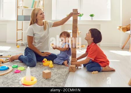Mutter und Söhne bauen im Zimmer einen Turm aus Holzwürfeln. Mutter unterrichtet Kinder am Tag der Auszeit zu Hause. Stockfoto