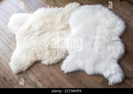 Natürliche Schafhaut und Synthetik auf dem Laminatboden im Raum. Blick von oben. Vergleich von Natur und Synthetik. Stockfoto