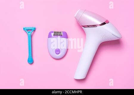 Violetter Epilierer, blauer Rasierer und Fotoepilator auf rosa Hintergrund. Blick von oben. Das Konzept der Wahl einer Methode der Haarentfernung. Stockfoto