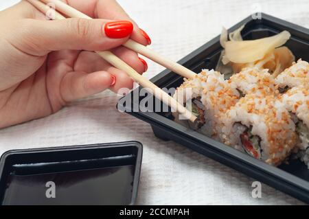 Frau essen zu Hause Sushi aus einem Behälter mit japanischen Sticks geliefert. Selektiver Fokus. Stockfoto