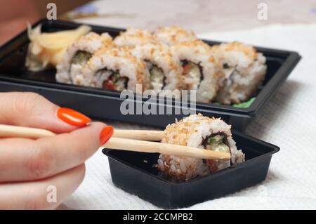 Frau essen zu Hause Sushi aus einem Behälter mit japanischen Sticks geliefert. Selektiver Fokus. Stockfoto