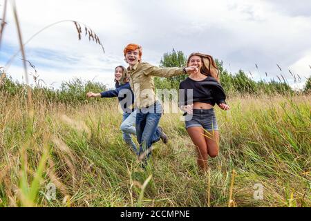 Sommerferien Urlaub glückliche Menschen Konzept. Gruppe von drei Freunden Junge und zwei Mädchen laufen und Spaß zusammen im Freien haben. Picknick mit Freunden auf dem Weg in die Natur Stockfoto