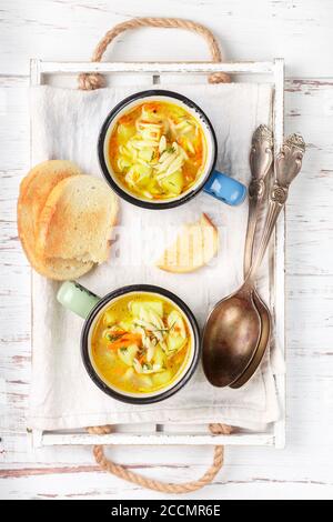 Hühnersuppe mit Kartoffeln, Karotten und Orzo-Nudeln in Keramikbechern auf einem Holztisch. Minestrone. Mediterrane (italienische) Küche. Selektiver Fokus Stockfoto