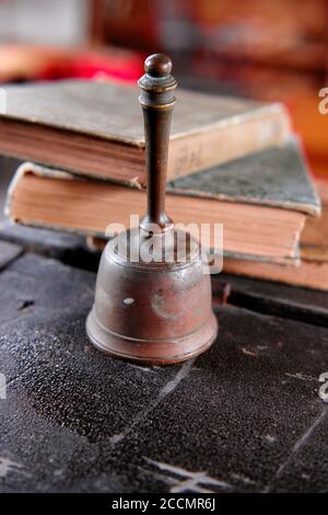 Eine antike Schulglocke sitzt auf dem Schreibtisch des Lehrers vor gut abgenutzten Schulbüchern. Stockfoto