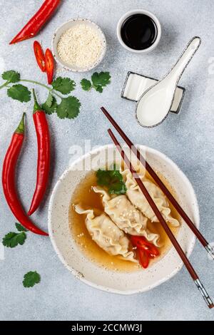 Frische heiße Suppe mit Knödeln (Gedza, Wontons) von Huhn, Schweinefleisch oder Garnelen mit Sojasauce, Chili, Koriander und Sesamsamen auf einem weißen Teller Stockfoto