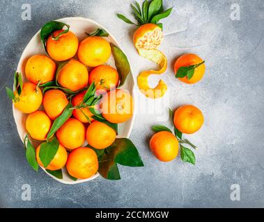 Frische Zitrusfrüchte Mandarine Orangen Frucht (Mandarinen, Clementinen,) mit Blättern in einer hellen Schale auf einem grauen Stein oder Beton Hintergrund. Selektiver Fokus, bis Stockfoto