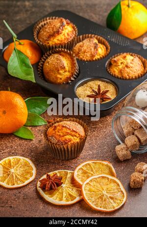 Frisch gebackene hausgemachte Zitrusfrüchte (Orange, Mandarine) Kuchen Muffins mit braunem Zucker, Zimt und Sternanis in schwarzem Teflon Backform über auf Holztabl Stockfoto