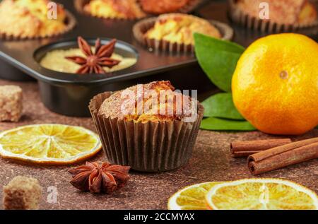 Frisch gebackene hausgemachte Zitrusfrüchte (Orange, Mandarine) Kuchen Muffins mit braunem Zucker, Zimt und Sternanis in schwarzem Teflon Backform über auf Holztabl Stockfoto
