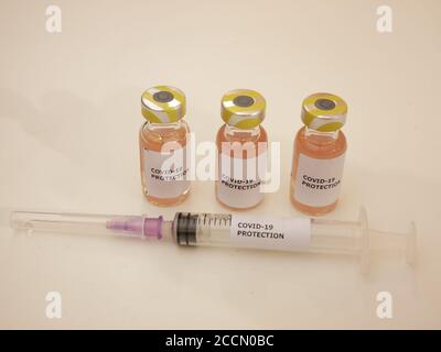 Impfstofffläschchen gegen Covid-19 mit Injektionsnadel und Schutz Gegen Coronavirus-Etikett mit hellem Hintergrund Stockfoto