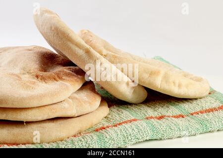 Frisch gebackenes Pita oder arabisches Brot auf einem rustikalen Tuch Und ein Holzbrett auf einer weißen Oberfläche Stockfoto