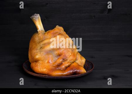 Gebratene Schweinshaxe in einer Tonkeramikplatte auf dunklem Holzhintergrund. Stockfoto