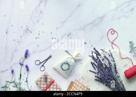 Aromatische trockene Lavendelbeutel verpackt in selbstgemachten umweltfreundlichen Geschenken. Frische und trockene Lavendelblüten. Flache Laie auf weißem Marmor. Stockfoto