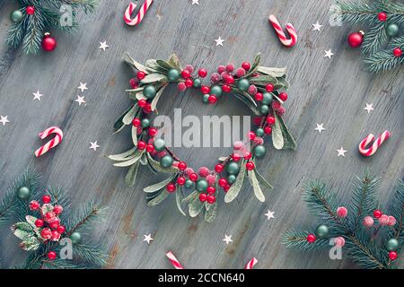 Dekorativer Mistelkranz in Herzform. Holz Weihnachten Hintergrund mit natürlichen Tannenzweigen, rot weiß Weihnachten stripy Süßigkeiten Stöcke und rot dekoriert Stockfoto