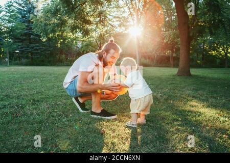 Junger Vater spielt Ball mit Kleinkind Baby Junge im Freien. Elternteil verbringt Zeit zusammen mit Kind Sohn im Park. Authentischer Lifestyle zarter Moment. Stockfoto