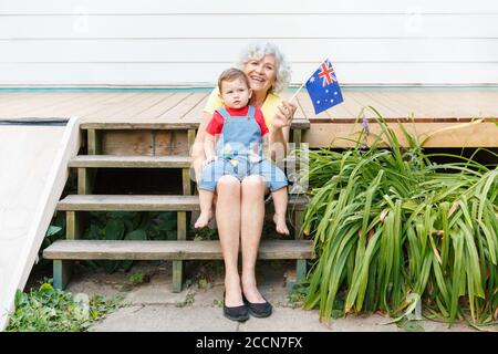 Glückliche alte Frau Großmutter mit Enkel Baby hält australische Flagge. Lächelnde alte Dame mit Kind auf dem Hinterhof winken Australien Flagge. Familie Stockfoto