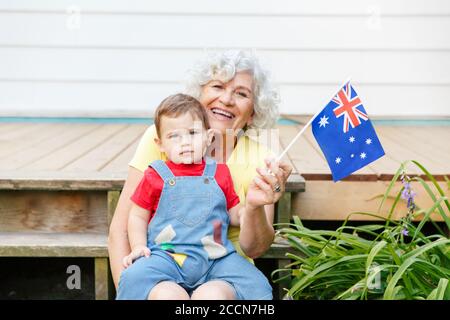 Glückliche alte Frau Großmutter mit Enkel Baby hält australische Flagge. Lächelnde alte Dame mit Kind auf dem Hinterhof winken Australien Flagge. Familie Stockfoto