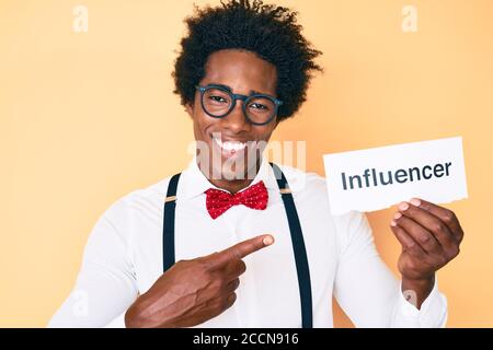 Schöner afroamerikanischer Mann mit afro Haar, das Papier mit hält Influencer Text lächelnd glücklich zeigen mit Hand und Finger Stockfoto