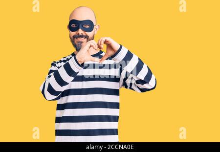 Junger schöner Mann trägt Einbrecher Maske lächelnd in der Liebe tun Herz Symbol-Form mit Händen. Romantisches Konzept. Stockfoto