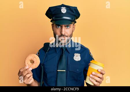 Gutaussehende hispanische Polizei Mann essen Donut und trinken Kaffee skeptisch und nervös, runzelte wegen des Problems. Negative Person. Stockfoto