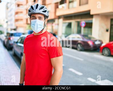 Junge Lieferung Mann trägt Fahrradhelm und Coronavirus Schutz medizinische Maske an der Straße der Stadt stehen. Stockfoto