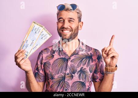 Junge gut aussehende blonde Tourist Mann mit Bart im Urlaub halten Bordkarte der Fluggesellschaft lächelnd, mit Hand und Finger zeigend Zur Seite Stockfoto