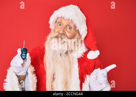 Alter älterer Mann mit grauen Haaren und langem Bart tragen santa claus Kostüm hält Auto Tasten lächelnd glücklich zeigen mit Hand und Finger zur Seite Stockfoto