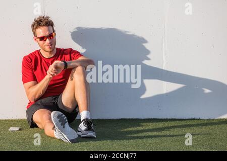 Smartwatch Sportman überprüft den Fortschritt auf der intelligenten Fitnessuhr nach dem Workout. Sportler in Sonnenbrillen entspannen mit Online-App auf Wearable Stockfoto