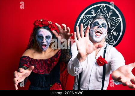 Schönes Paar trägt Tag der Toten Kostüm gestikuliert als Zombie über isolierten roten Hintergrund. Stockfoto