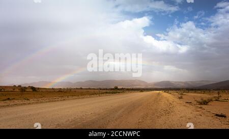 Doppelter Regenbogen in der Wüste nach dem Regen. Nicht versiegelte Straße. Dramatische Himmel dunklen Wolken. Berge im Hintergrund. Flinders Ranges, Australien Stockfoto