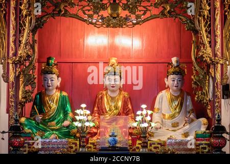 Altar mit drei sitzenden Statuen in einem viet-Tempel. Geister von drei Gottheiten. Roter Holzhintergrund. Goldene Details. Pagode Vĩnh Nghiêm, Vietnam Stockfoto