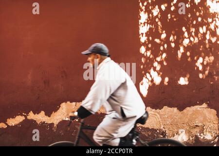 MARRAKESCH, MAROKKO - 10. SEPTEMBER 2019: Verschwommener Einheimischer, der Fahrrad auf der Marrake-Straße fährt. Rote Stadt, Terrakotta-Hintergrund. Marokkanisches Leben. Stockfoto