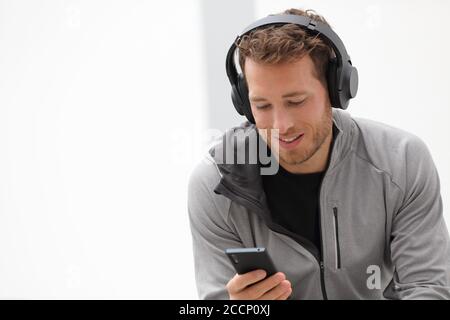 Mann hört Musik Handy-App tragen Headset zu Hause sitzen. Gesunder Lifestyle-Sportler mit Smartphone auf Jogging-Pause im Freien Stockfoto