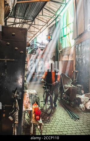 MARRAKESCH, MAROKKO - 10. SEPTEMBER 2019: Lokaler marokkaner fährt mit dem Fahrrad durch Souk Medina Markt in Marrakesch. Erstaunliche Sonne Licht und Strahlen. Traditioneller arabischer Markt. Stockfoto