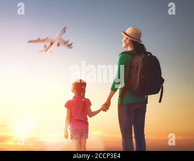 Glückliche Familie bei Sonnenuntergang. Mutter und ihr Kind Tochter Blick auf das fliegende Flugzeug in den Himmel. Stockfoto
