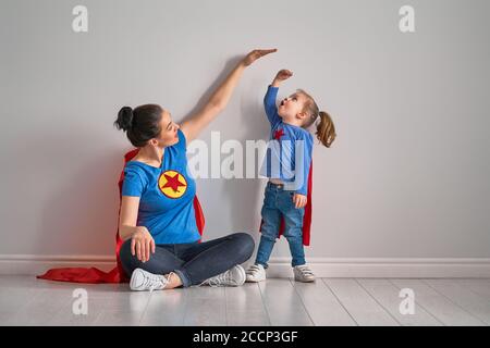 Mutter misst das Wachstum der Tochter in der Nähe einer leeren Wand. Mädchen in Superhelden Kostüm. Stockfoto