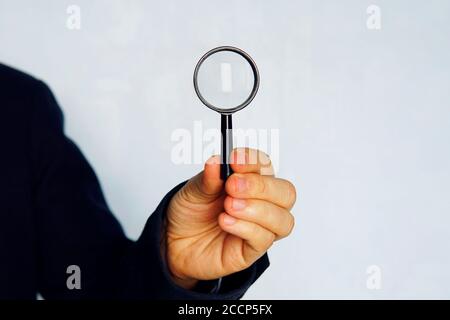 Konzept der Suche. Nahaufnahme des Geschäftsmannes in blauem Anzug mit Lupe auf blauem Hintergrund Stockfoto